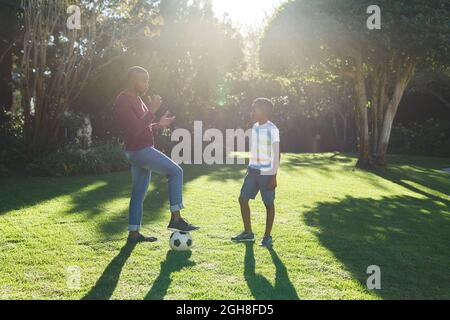 African american father talking with son and playing football in garden Stock Photo