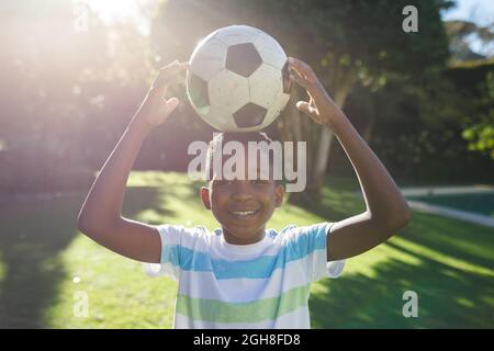 Portrait of smiling african american boy having fun and playing with football in garden Stock Photo