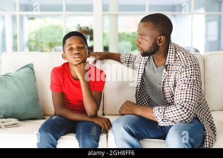 African american father sitting on couch talking to son in living room Stock Photo