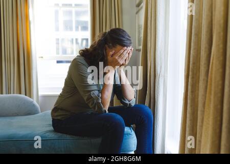 Stressed senior caucasian woman sitting on sofa by window covering face Stock Photo