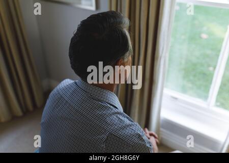Thoughtful senior caucasian man sitting on sofa and looking through window Stock Photo