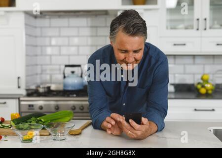Smiling senior caucasian man in modern kitchen, using smartphone Stock Photo