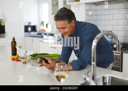 Smiling senior caucasian man in modern kitchen, using smartphone Stock Photo