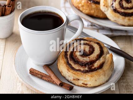 Cinnamon roll with cup of coffee and cinnamon sticks on a plate Stock Photo