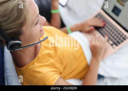 Woman in headphones with microphone lies on bed and works on laptop Stock Photo