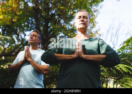 Peaceful senior caucasian couple practicing yoga, meditating in sunny garden Stock Photo