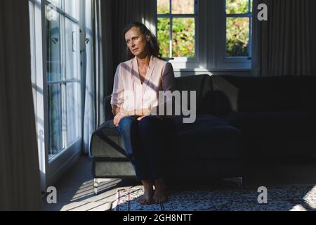Thoughtful senior caucasian woman in bedroom, looking through window Stock Photo