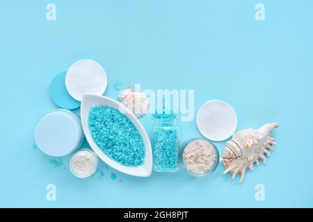 Sea salt, cream, sponges and shells in cosmetics set for spa on blue background. Top view with space for text Stock Photo