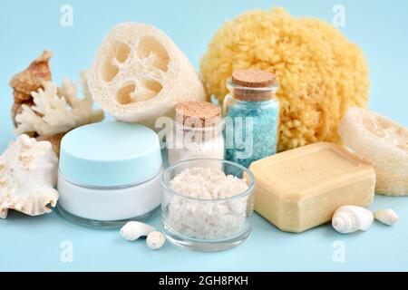 Spa accessories - sea salt, cream, sea sponge, soap and shells in cosmetics set for spa on blue background. Healthy lifestyle concept. Stock Photo