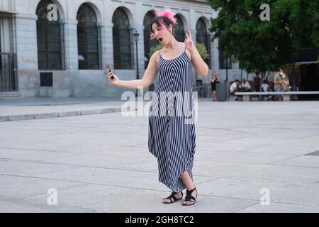 Young caucasian woman with pink hair taking a selfie in street with earbuds. Stock Photo