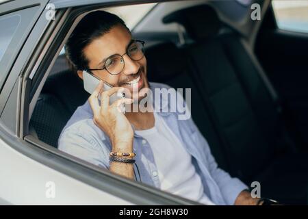 Cheerful indian man sitting in taxi, talking on cellphone Stock Photo