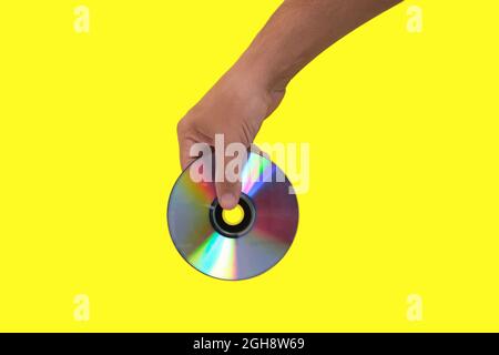 Scratched CD in your hand on a yellow background, outdated technologies Stock Photo