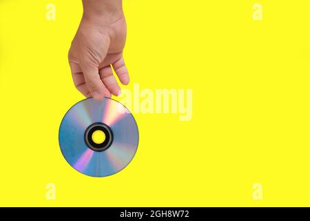 Scratched CD in your hand on a yellow background, outdated technologies Stock Photo