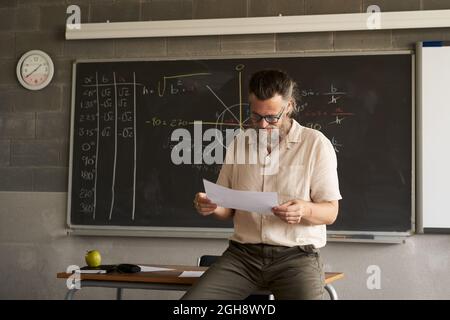 Male teacher prepares or corrects exams in the classroom. Stock Photo