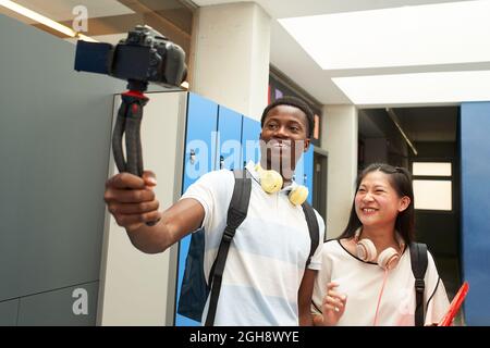Interracial student couple making a video for social media. Selfie of two young people taking selfie in high school with a video camera. Vlogging. Stock Photo