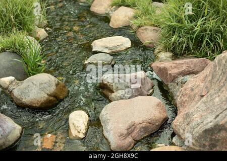 Water runs over the stones. Fresh water stream. Artificial waterfall. Landscaping on the territory. Stock Photo