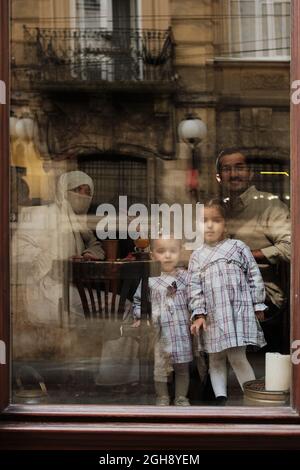 LVIV, UKRAINE - September 6, 2021. Arabic Happy Family drink coffe. People sit inside the cafe in Lviv, Ukraine. Photo through the window Stock Photo