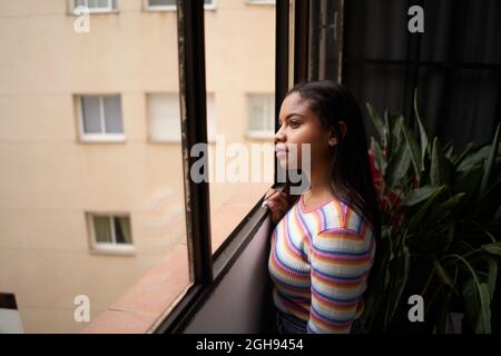 African American girl near the window. From home looking outside with a smile.