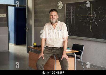 Middle-aged bearded male teacher looking at camera in the classroom. Happy and engaged teacher. Stock Photo