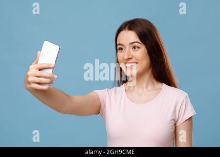 Attractive young lady taking selfie on blue studio background Stock Photo