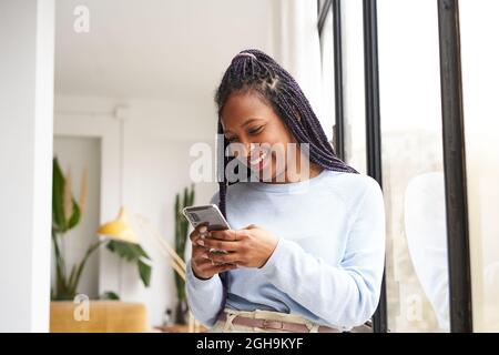 Young African American woman using a smart phone at home, near the window. Concept of youth and online communication. Stock Photo