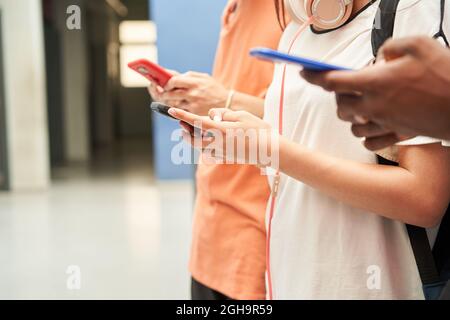 Close up of the hands of a multiethnic group of unrecognizable students using a smart phone. Connected, smiling people. Stock Photo