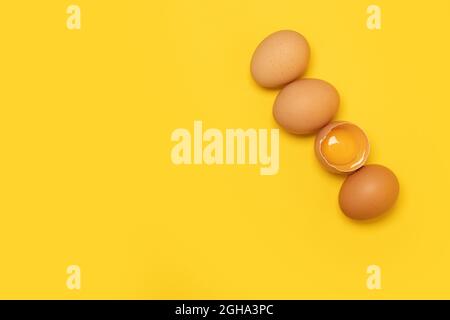 Raw brown chicken eggs and one broken egg with yolk on yellow background Stock Photo