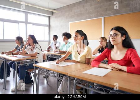 Group of students of different ethnicities sitting in class attending to the teacher. Young people studying at the college sitting at their desks. Stock Photo