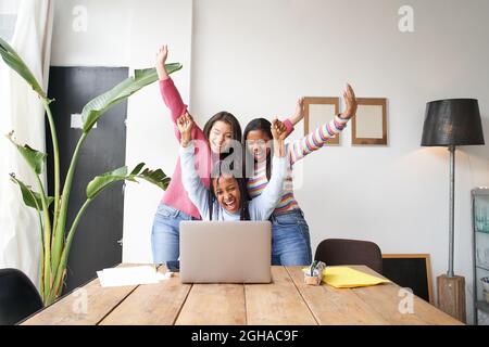 A work team of young women celebrate good news in front of the computer. Multi-ethnic group of empowered women congratulate each other on success. Stock Photo