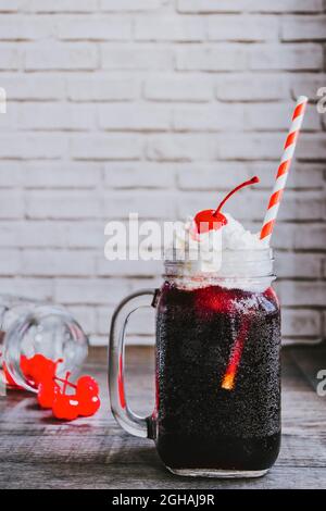 Non-alcoholic cocktail 'Cherry Coke Float' made from cherry syrup and coke, decorated with vanilla ice cream and cherry, served in glass jar. Stock Photo