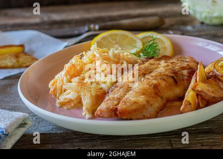Breaded fish with coleslaw on a plate on wooden table. closeup and front view Stock Photo