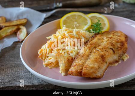 Breaded fish with coleslaw on a plate on wooden table. closeup and front view Stock Photo