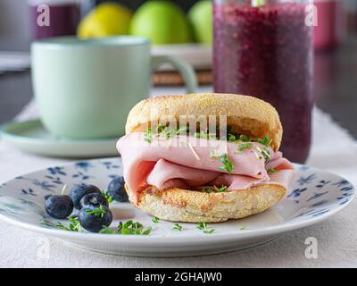 Healthy breakfast sandwich made with toasted english muffin and thin sliced ham served with a fresh blueberry smoothie and a cup of coffee on a table Stock Photo