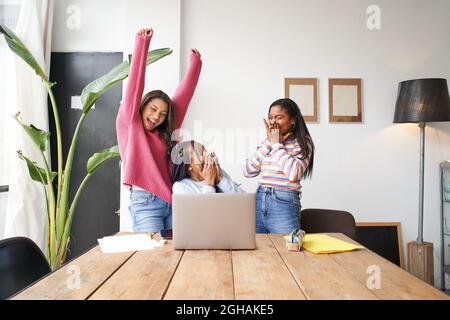 Excited businesswomen raising hands celebrating incredible online results, happy partners motivated by great achievements or team victory, amazed by Stock Photo