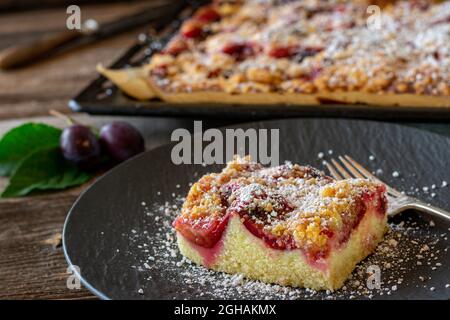 Plum cake with crumbles on wooden table with whole sheet cake in the background Stock Photo
