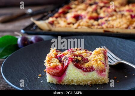 Piece of homemade plum crumble cake on wooden table. Delicious juicy sheet cake Stock Photo