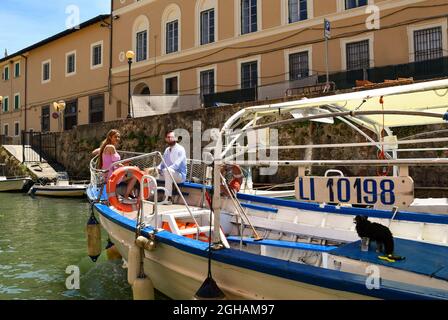 A woman, a man and a little dog on board of a boat sailing in a canal of the New Venice district in summer, Livorno, Tuscany, Italy Stock Photo