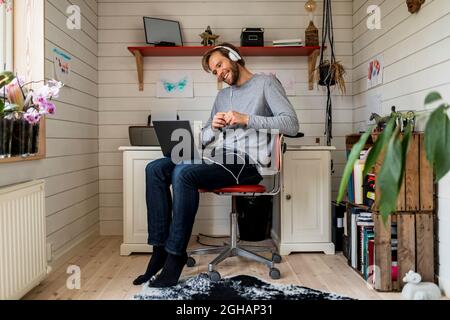 Full length of smiling man wearing headphones while doing video call through laptop at home Stock Photo
