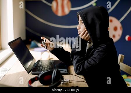Autistic boy with hand on chin looking at laptop in bedroom Stock Photo
