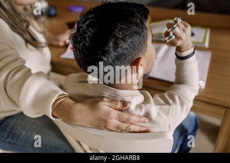Autistic son with arm fist sitting by mother in living room Stock Photo