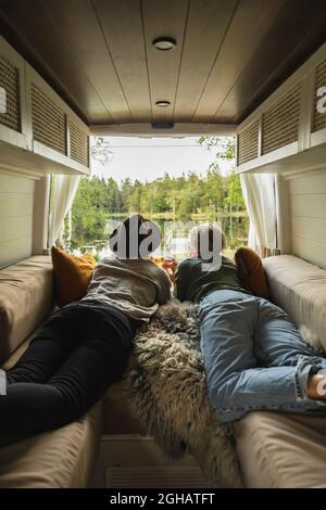 Rear view of couple looking at view while lying down in camping van Stock Photo