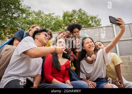 Group of multi-ethnic students taking selfies with mobile phone. Teenagers using a smart phone and having fun together. Stock Photo