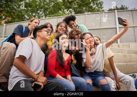 Group of multiracial students taking selfies with mobile phone. Chinese girl shows her fingers Stock Photo