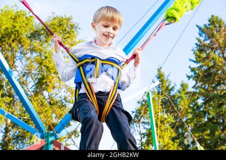 Happy Kid Jumping on the Trampoline with a Rubber Ropes in the Park Stock Photo