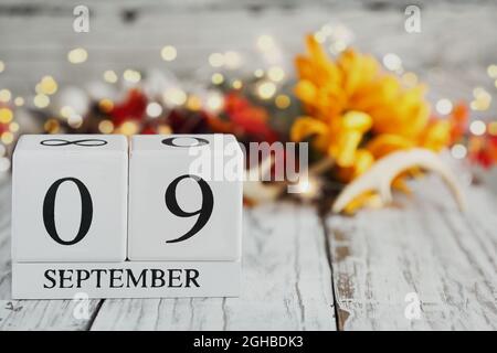 Generic white wood calendar blocks with the date September 9th and autumn decorations over a wooden table. Selective focus with blurred background. Stock Photo