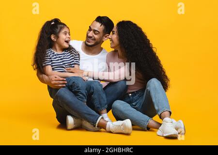 Cheerful Arab Parents Having Fun With Little Daughter Over Yellow Studio Background Stock Photo
