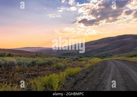 A dirt road that runs through a valley towards the setting sun in northwest colorado. Small anti crepuscular rays are visible in the upper area. Stock Photo