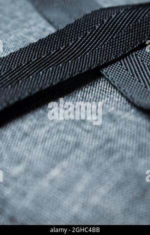 Close up of a grey polyester backpack background and some black straps going through it Stock Photo