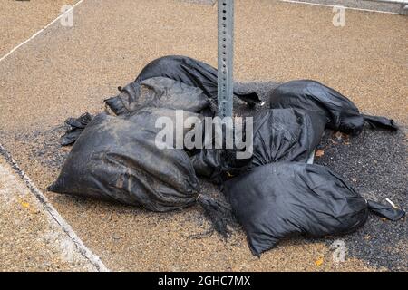 Black woven plastic bags filled with asphalt slag supporting the base of a temporary street sign, aggregate sidewalk, horizontal aspect Stock Photo