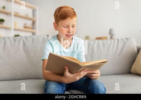Cute redhead boy sitting at home, reading book Stock Photo